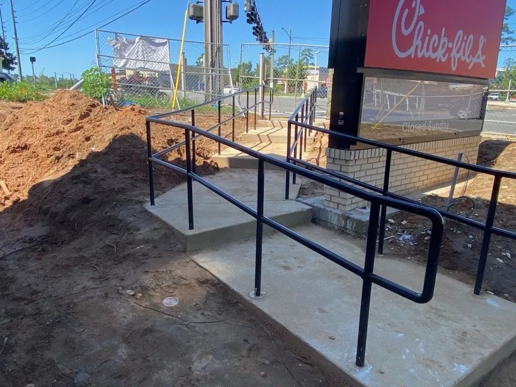Concrete ramp with black handrails leading to Chick-fil-A sign, construction site.