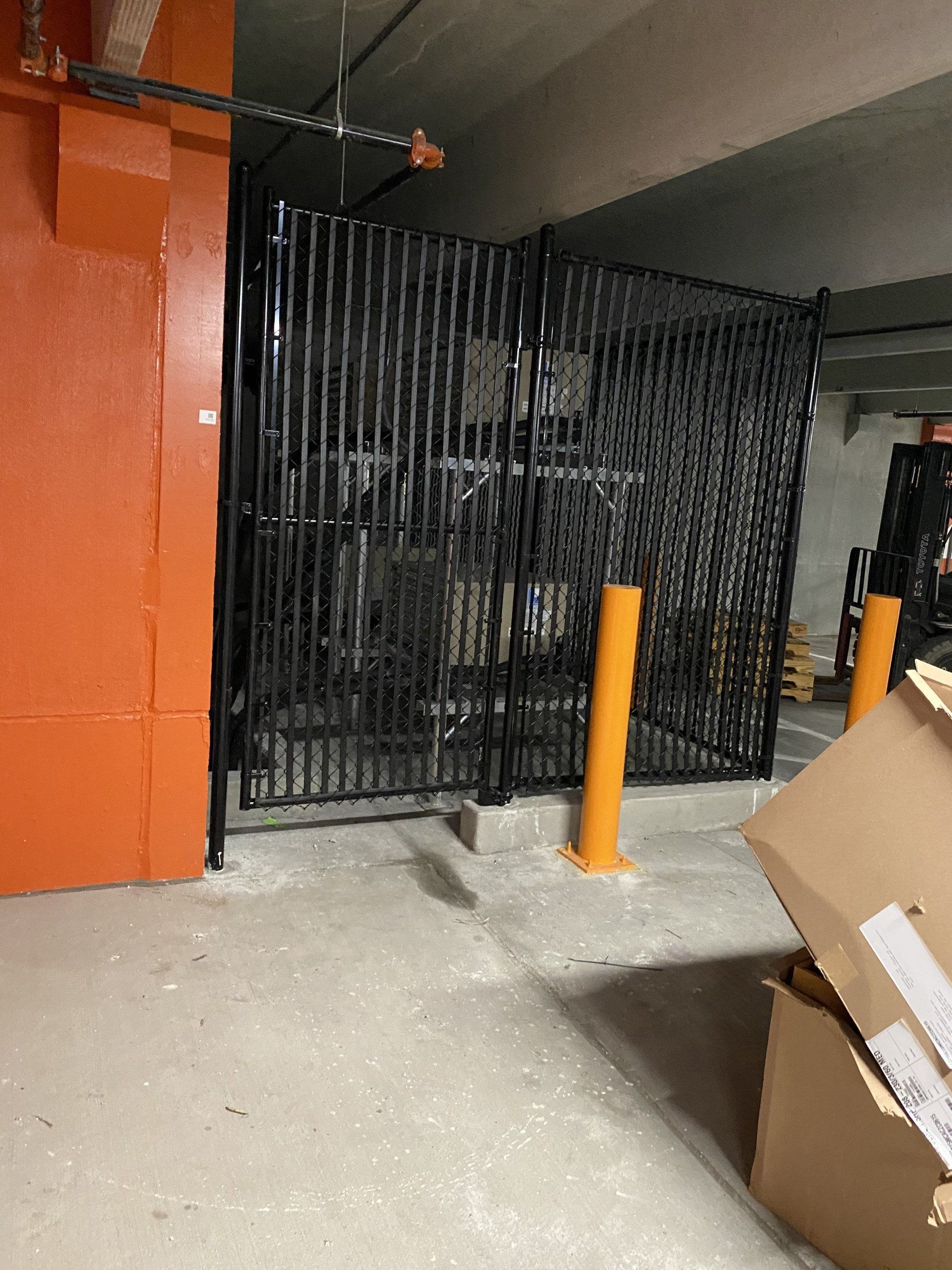 Black metal security gate in a concrete parking garage, with orange support columns and boxes.