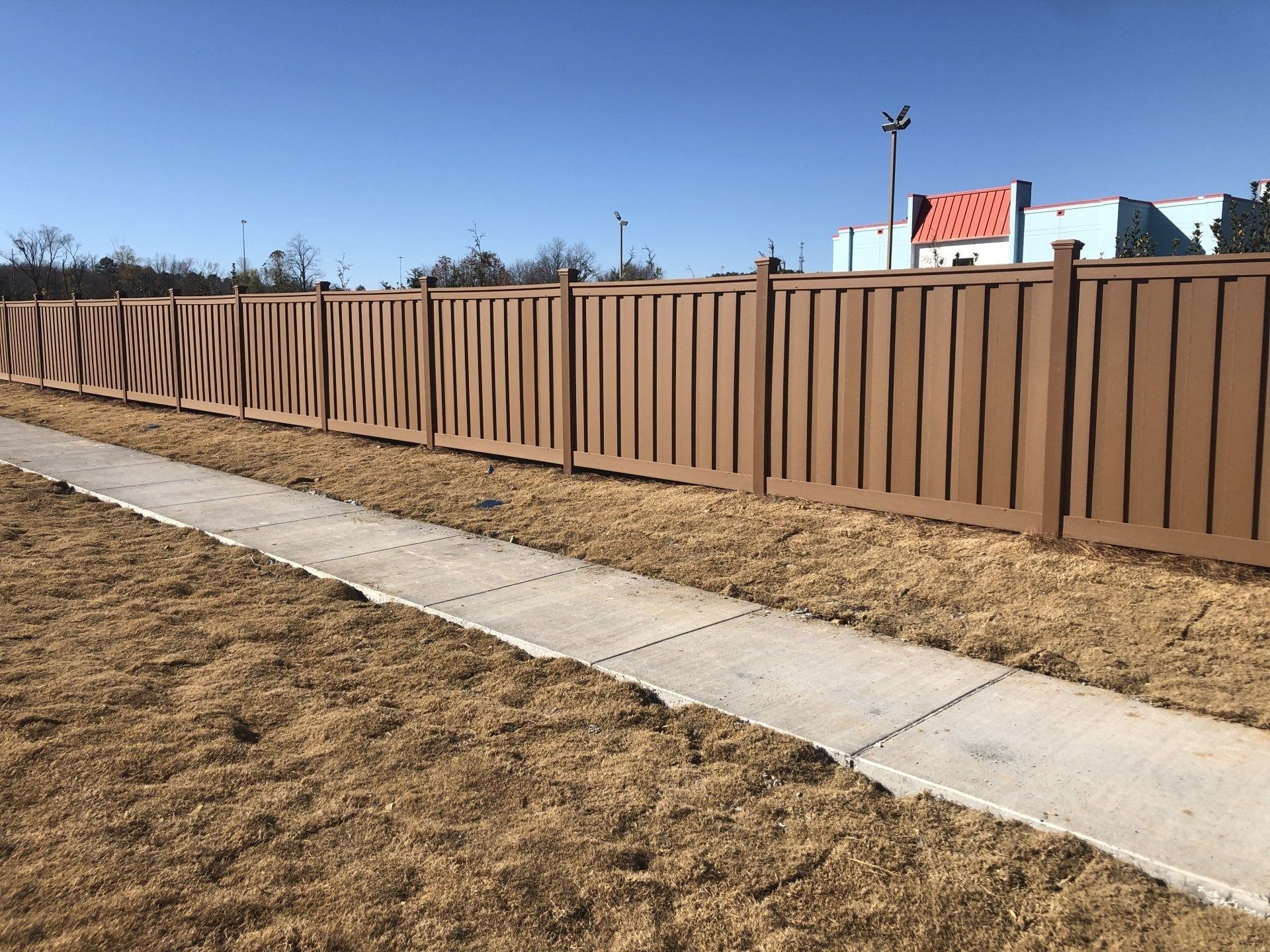 Brown wooden fence beside a concrete sidewalk on a sunny day.