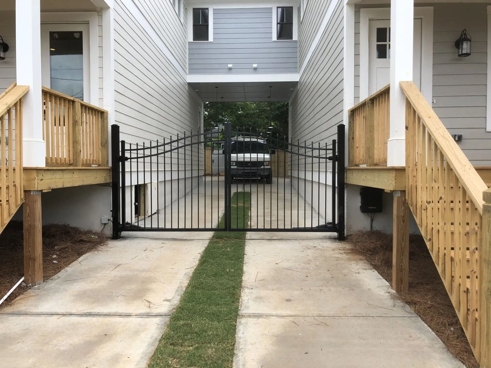 Driveway between two buildings, black iron gate, car in the distance.