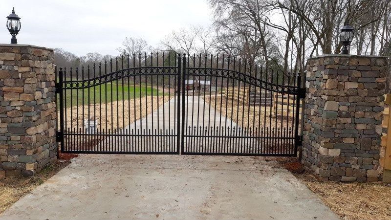 Black metal driveway gates between stone pillars with lamps.