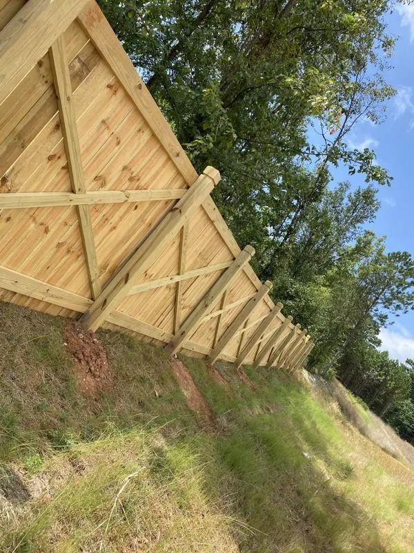 Wooden fence built on a hillside; triangular panels are supported by posts and cross beams.