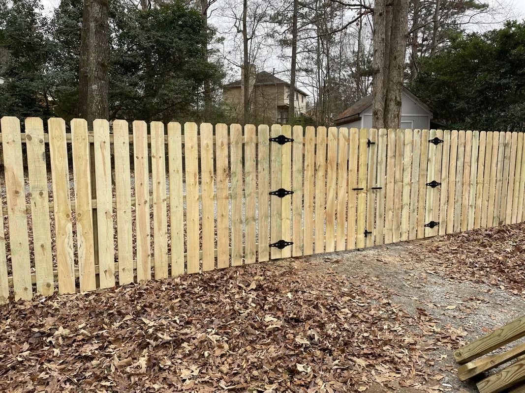 Wooden fence with three black metal gates in a wooded area.