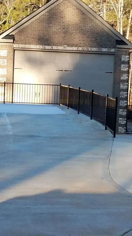 Exterior view of a garage with a concrete driveway and black metal fence.