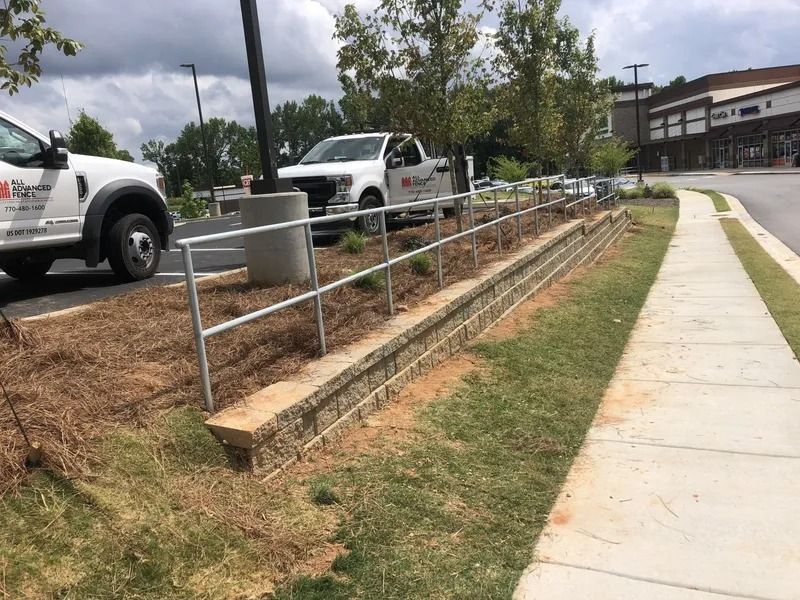 A low brick wall with a metal railing alongside a sidewalk, with two white work trucks parked nearby.