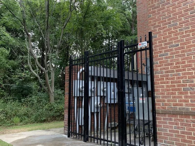Black metal gate enclosing electrical equipment next to a brick building.