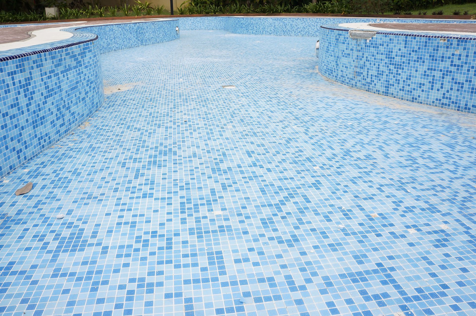 Empty swimming pool tiled with blue and white mosaic tiles.