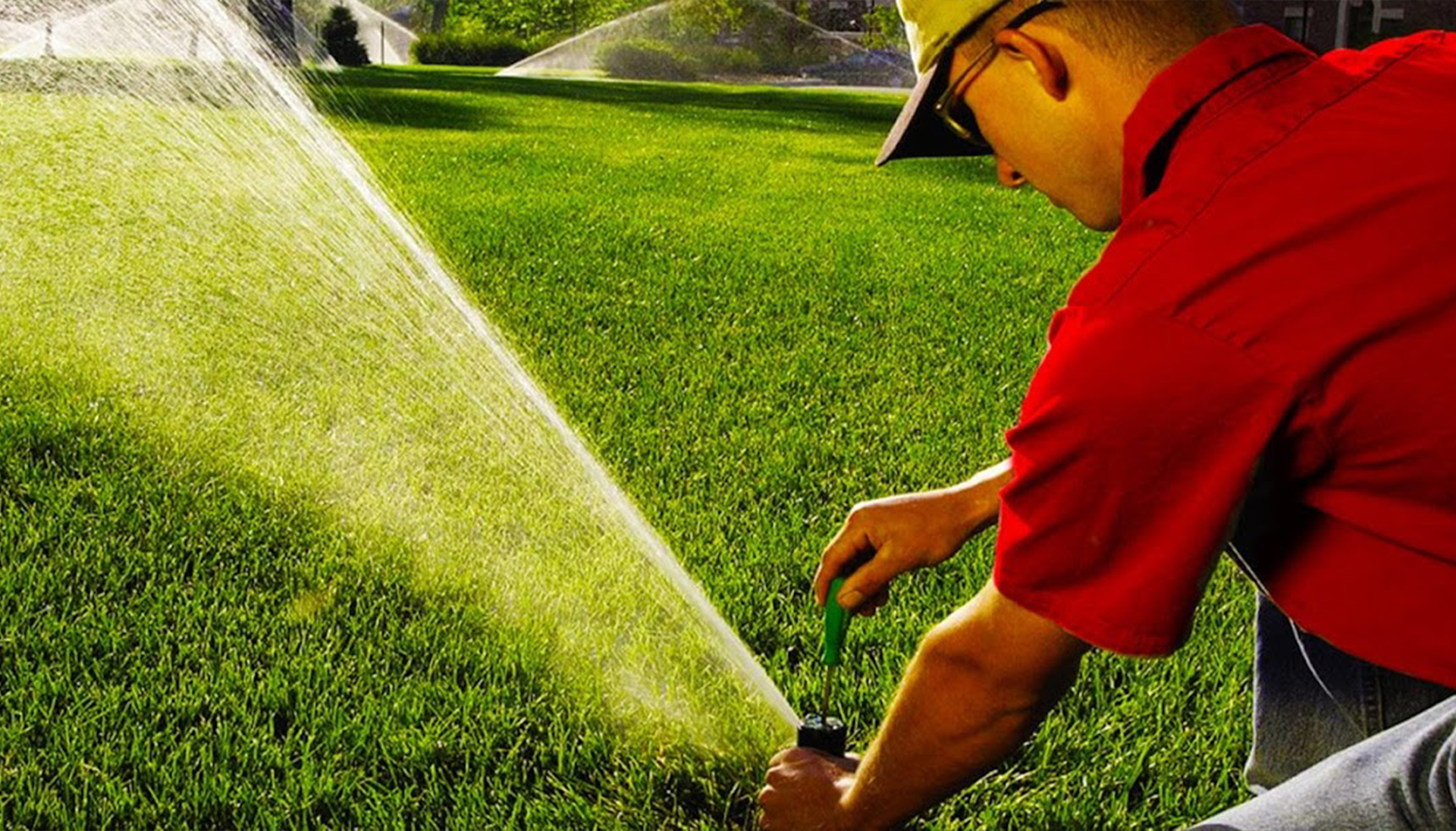 Man adjusts sprinkler head on green lawn.