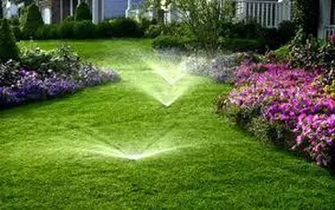 Lawn sprinkler system watering lush green grass and flower beds in a garden.