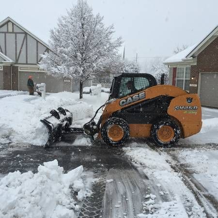 A Case skid steer clears snow from a driveway in a residential neighborhood.