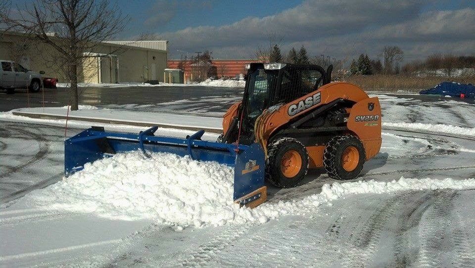 Orange Case skid steer plowing snow in a parking lot. Blue plow blade.