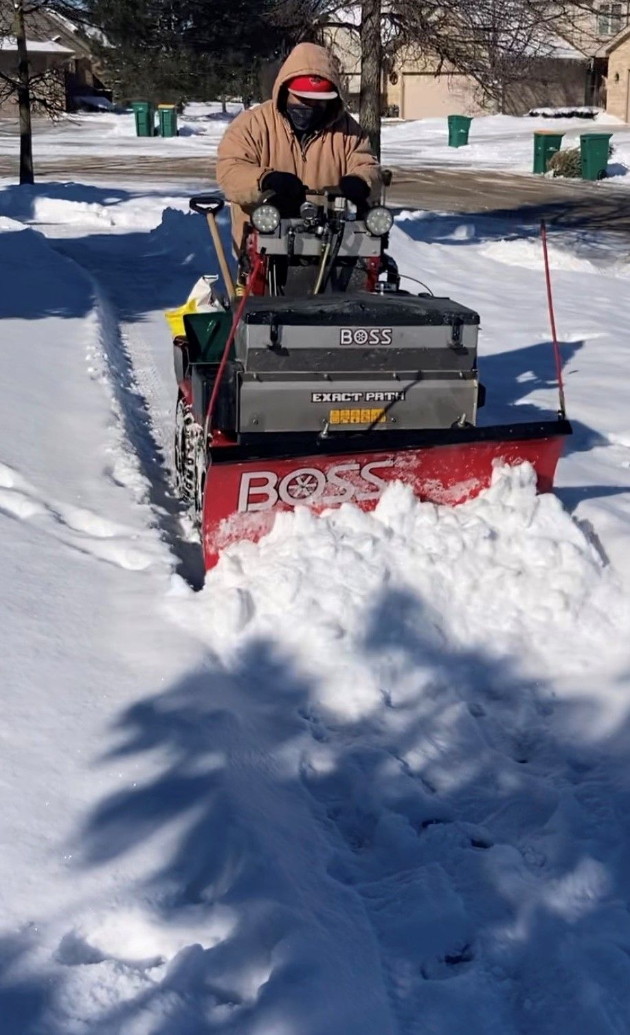 Person in winter gear operating a red BOSS snowblower, clearing a snowy residential street.