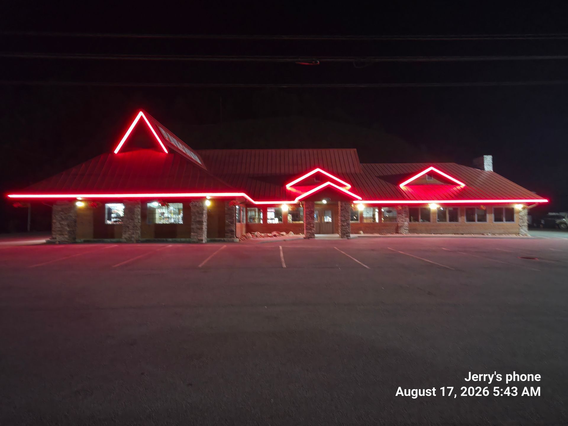 Nighttime exterior of a lit building with red roof lights and an empty parking lot