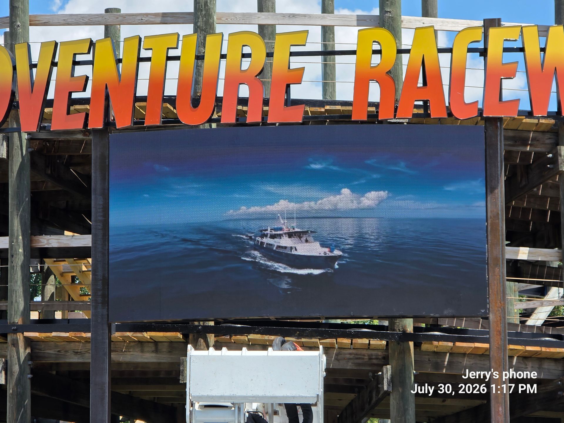 Adventure race event sign with a large screen showing a boat on blue water at sunset
