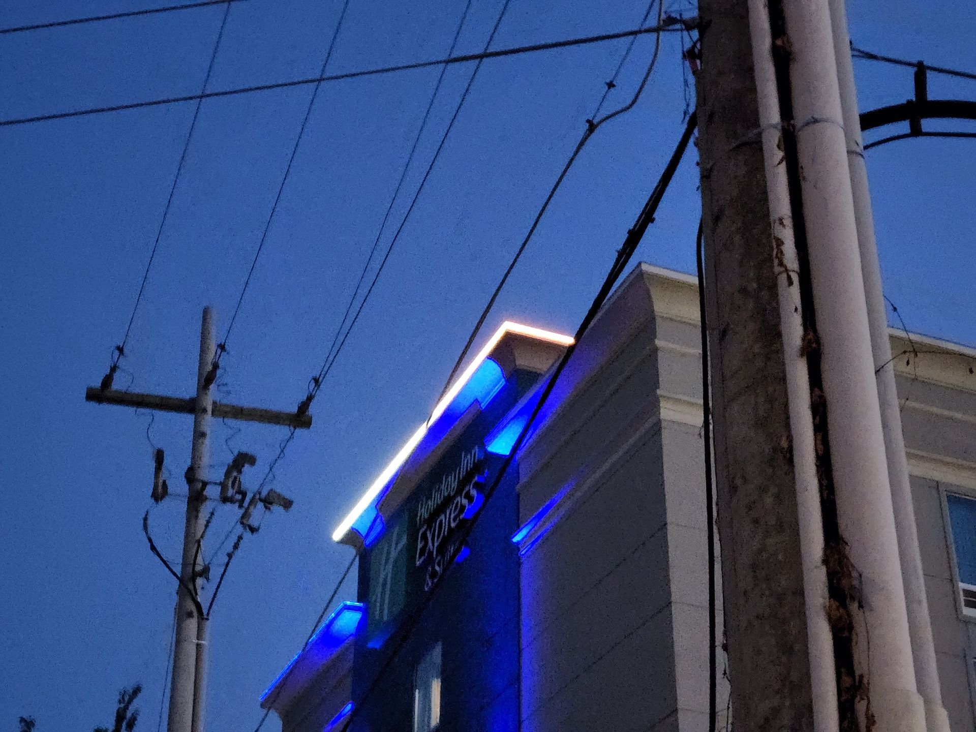 Blue-lit building at dusk with power lines and utility poles overhead