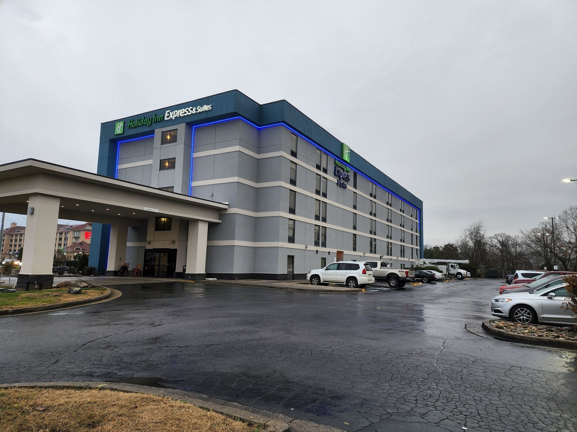 Exterior of a gray hotel with a blue roofline on a wet day, with parked cars and an entrance canopy