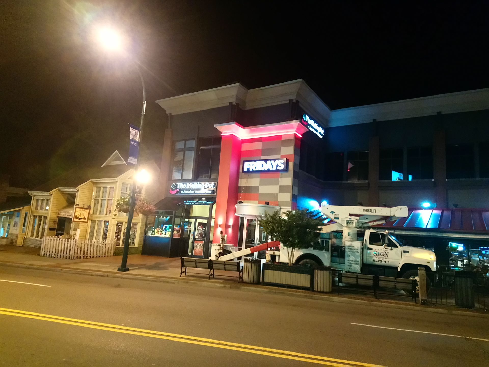 Night street view of a brightly lit restaurant with red signage and parked vehicles outside