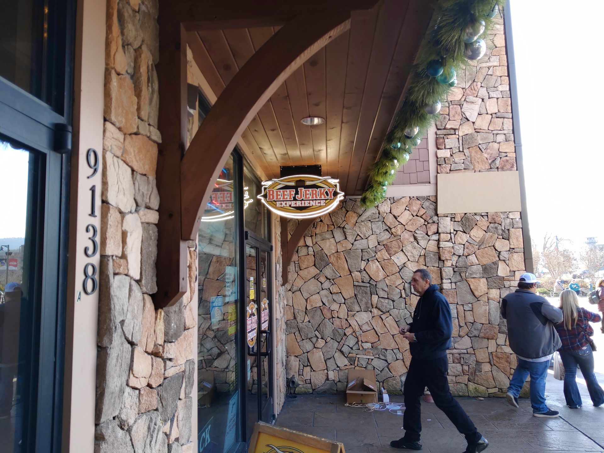 People walking beside a stone storefront with a wooden overhang and hanging sign.