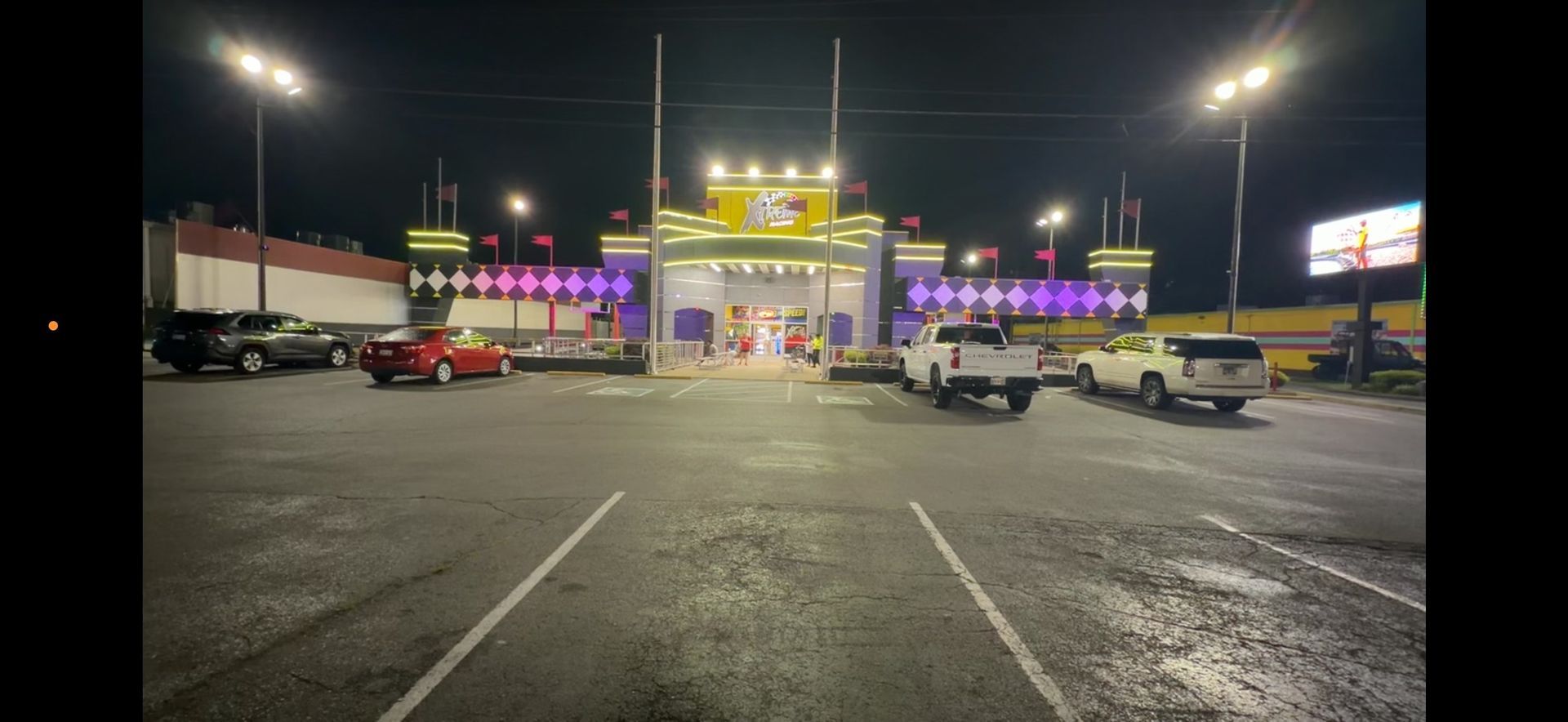 Nighttime parking lot outside a brightly lit gas station and convenience store, with cars parked nearby.
