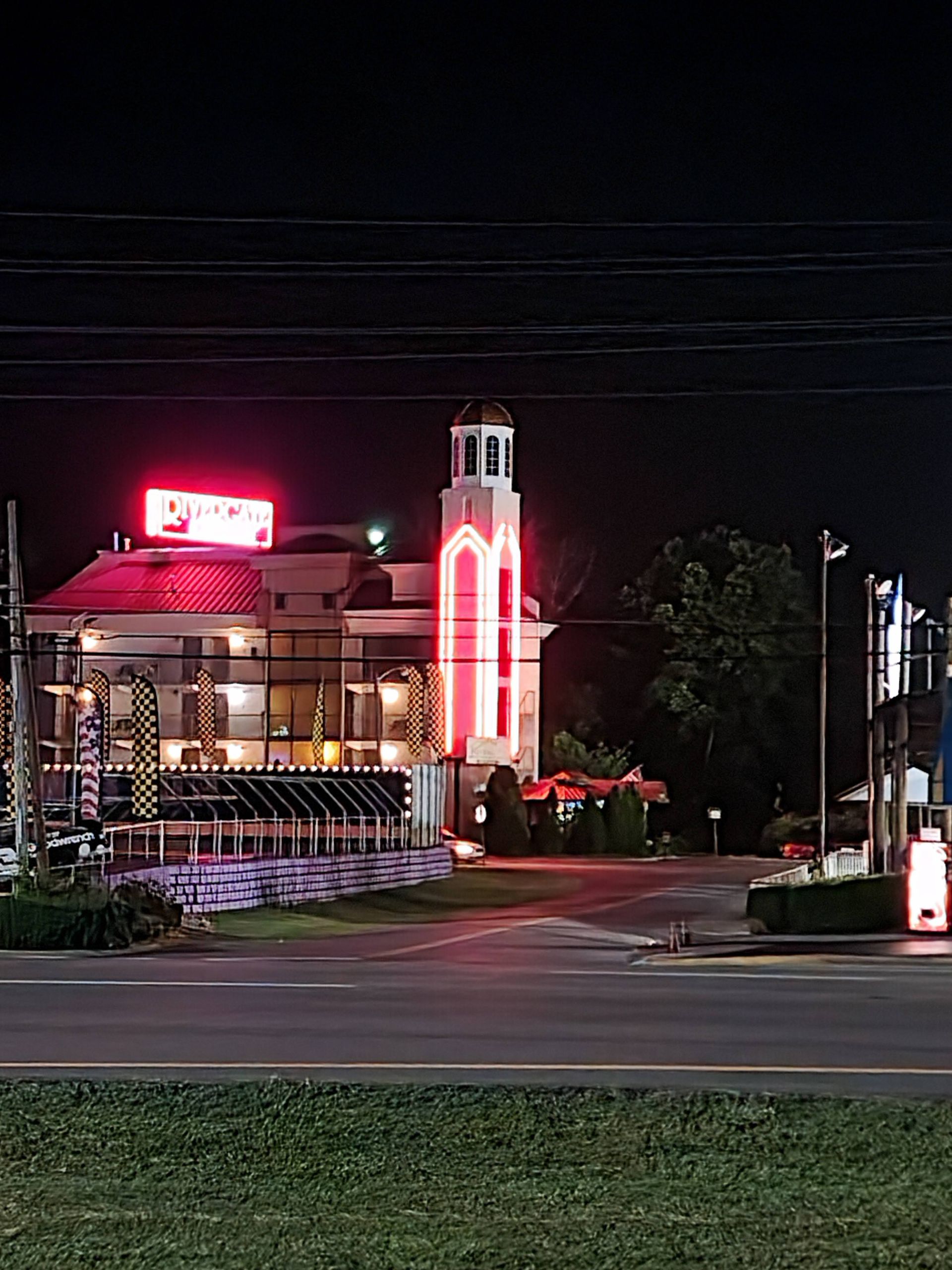 Nighttime view of a neon-lit building with a tower, viewed from across a mostly empty road.