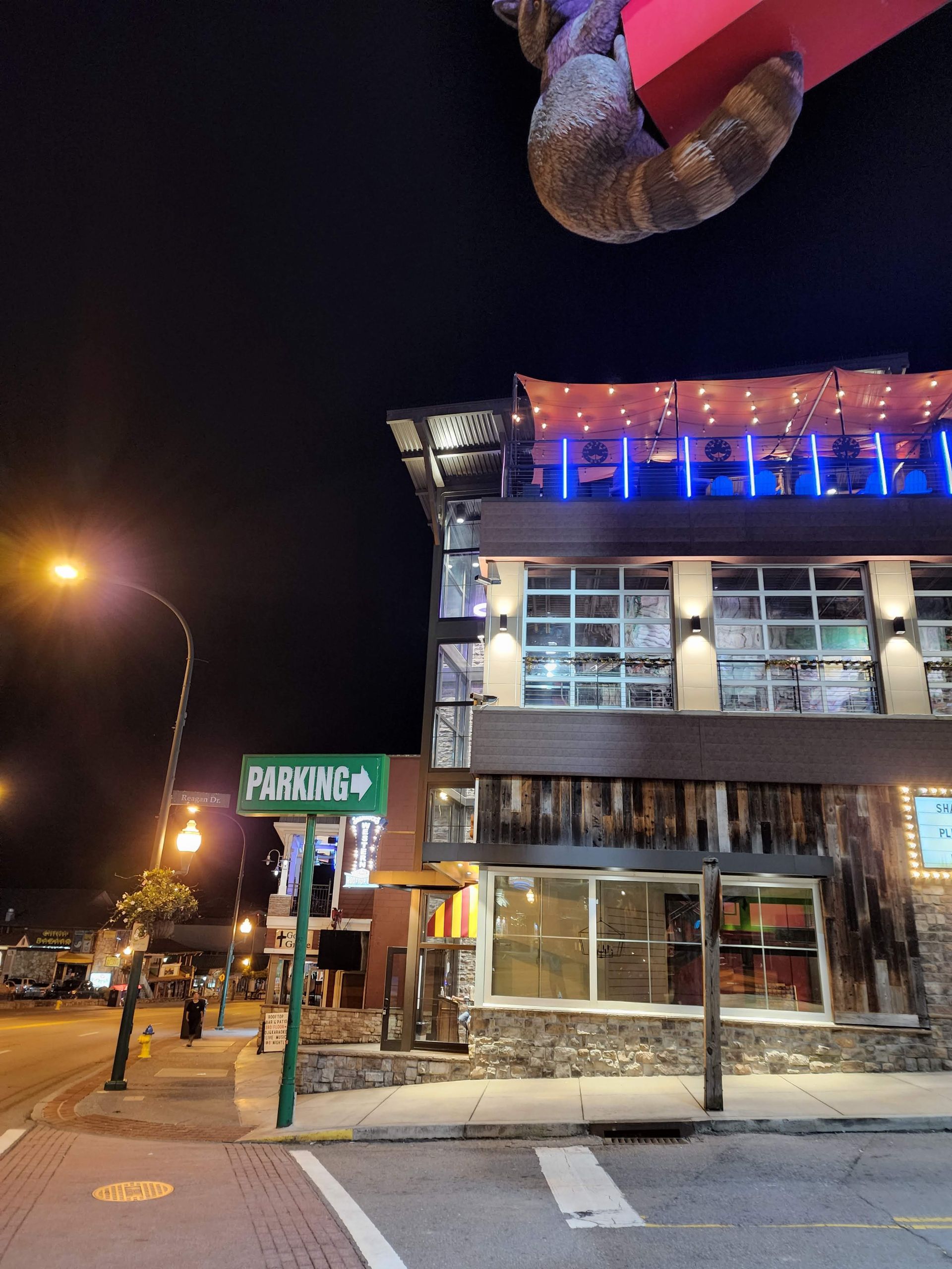 Nighttime street view of a lit storefront with blue and orange lights on a corner building, snowy sidewalk.
