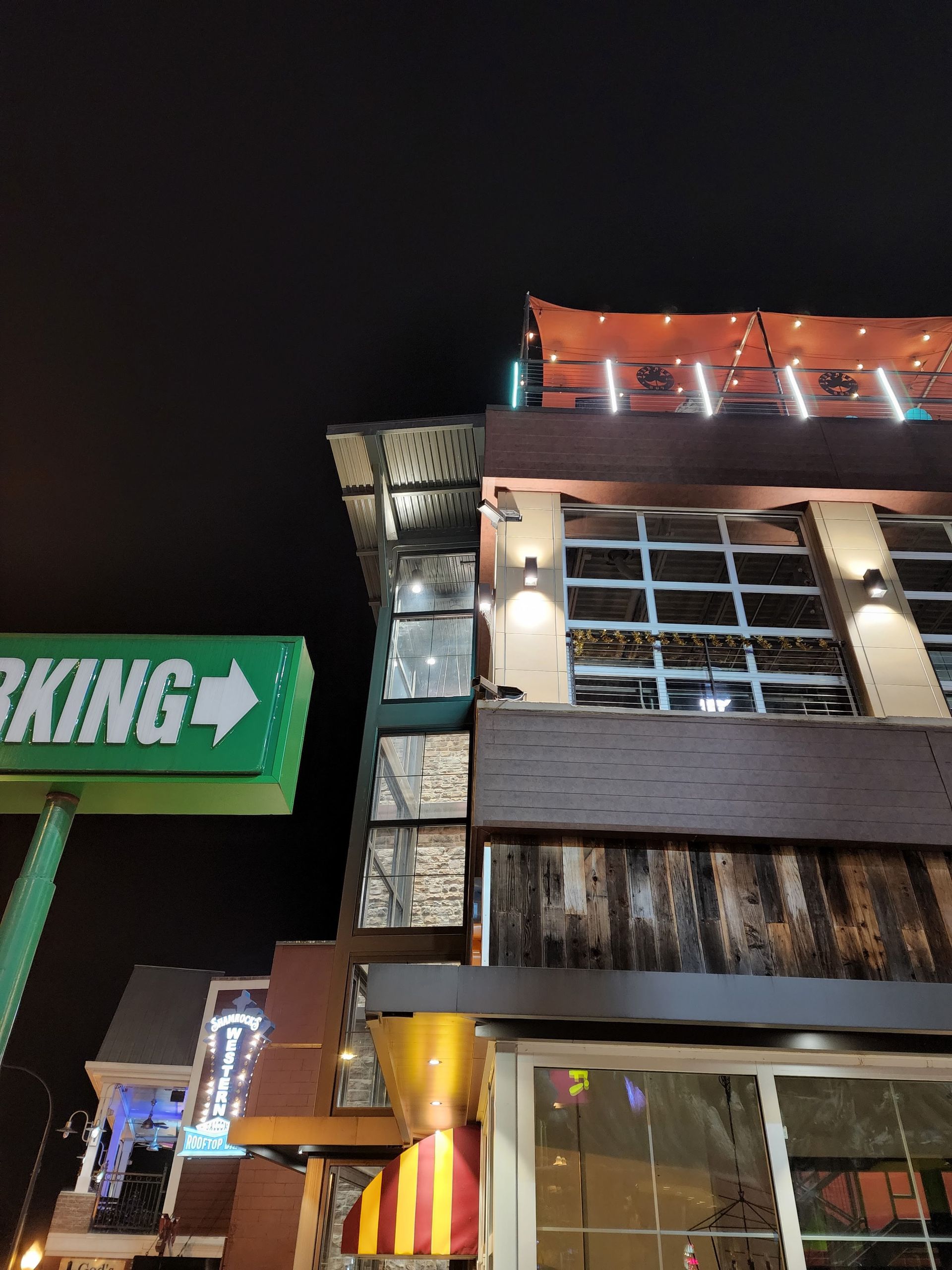Nighttime view of a brightly lit building facade with a green parking sign and orange-striped awning