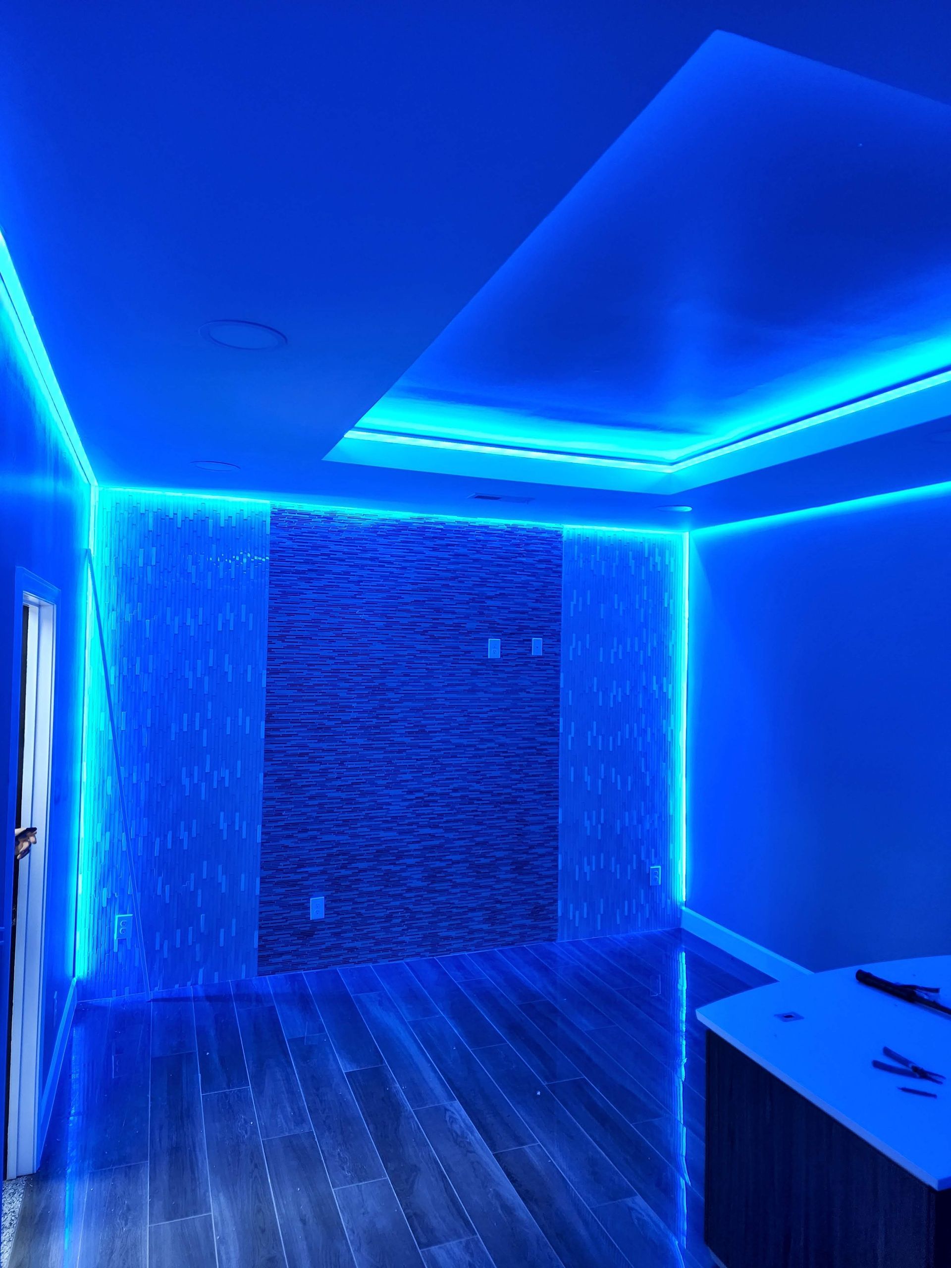 Blue-lit empty modern room with recessed ceiling lights, textured wall, and dark wood floor.