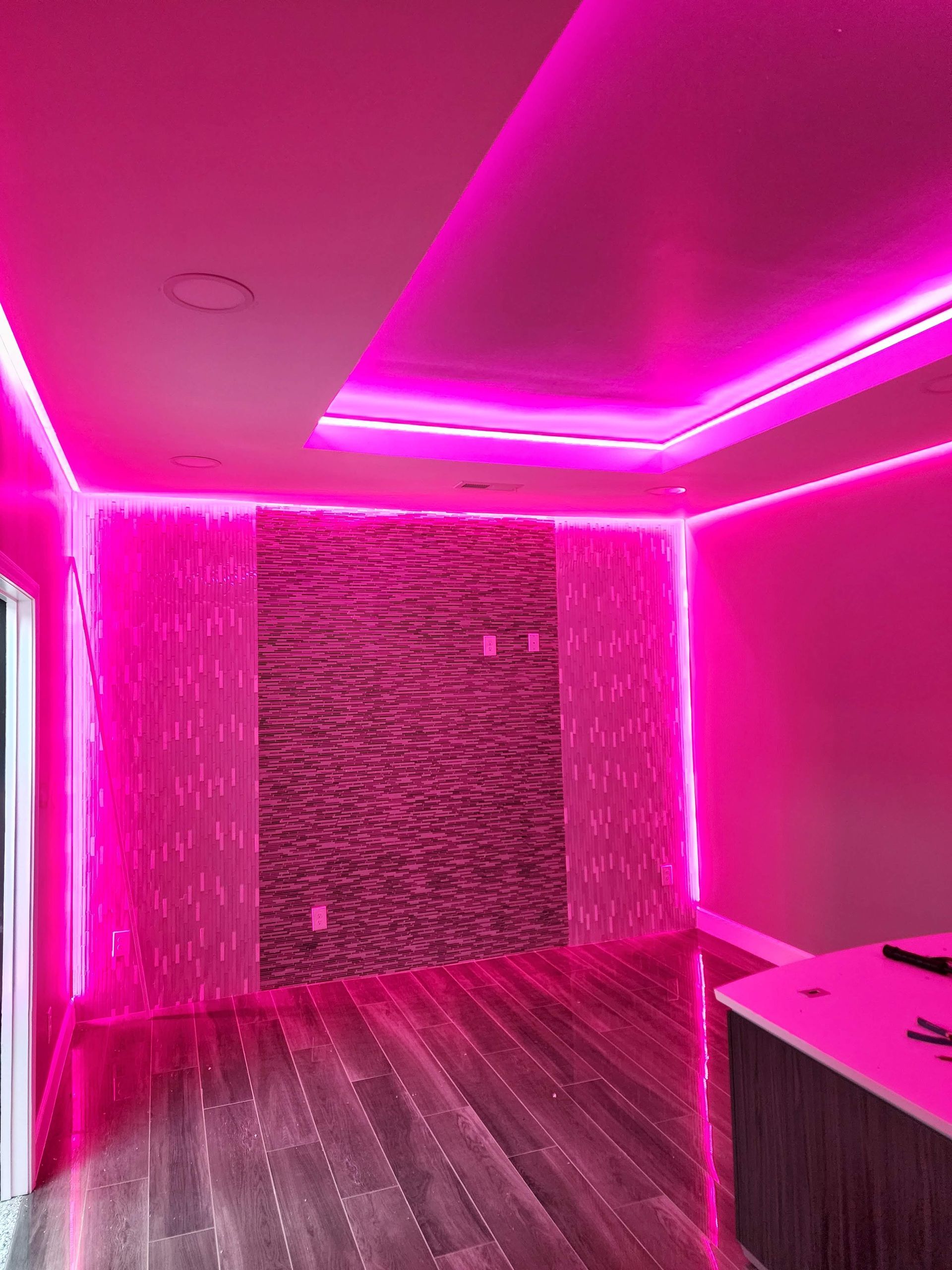 Neon pink-lit room with textured accent wall, wood floor, and desk in the corner.