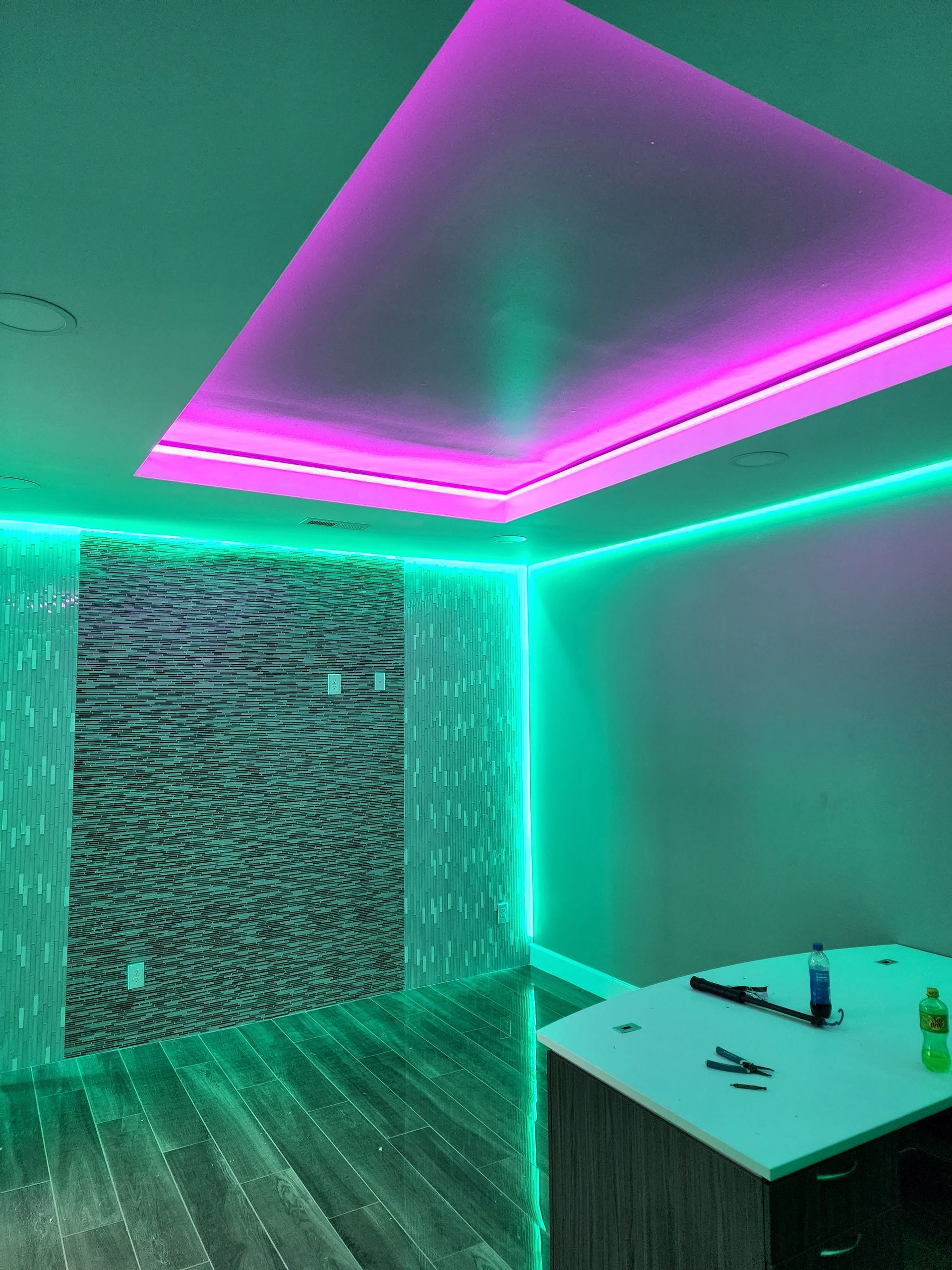 Neon-lit room with green and pink LED ceiling lights, a table, and a textured wall panel.