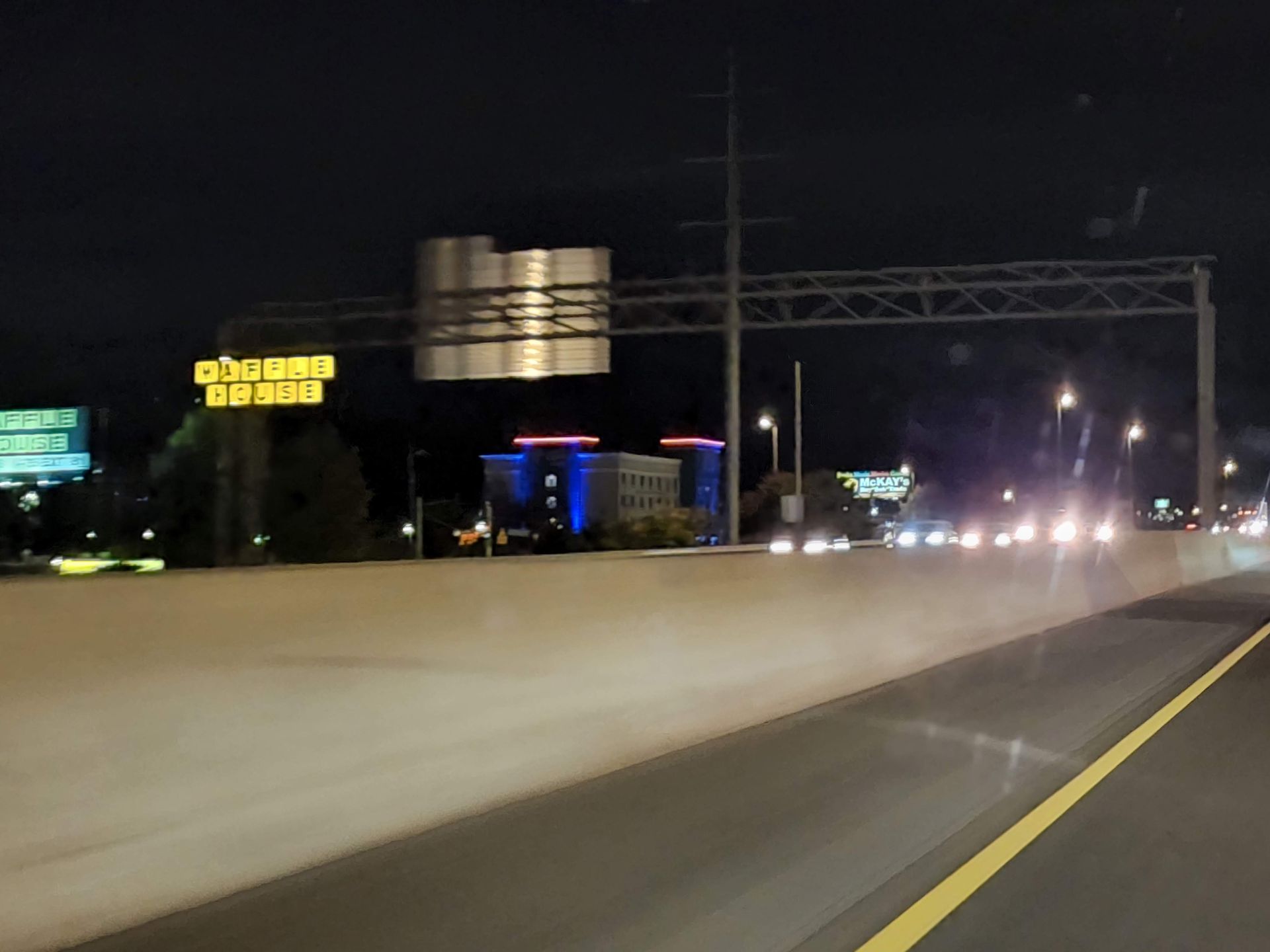 Night highway scene with headlights, concrete barrier, and a lit sign in the distance