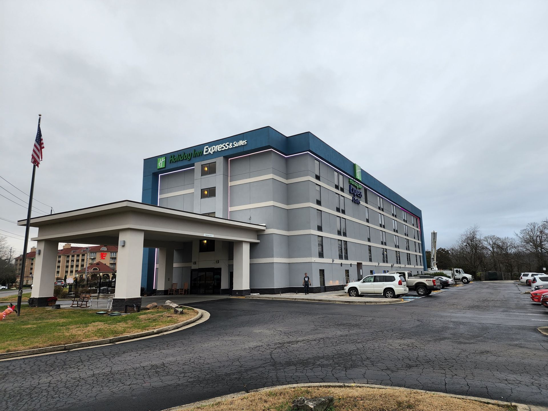 Exterior of a Holiday Inn hotel with covered entrance, American flag, and parked vehicles on a cloudy day