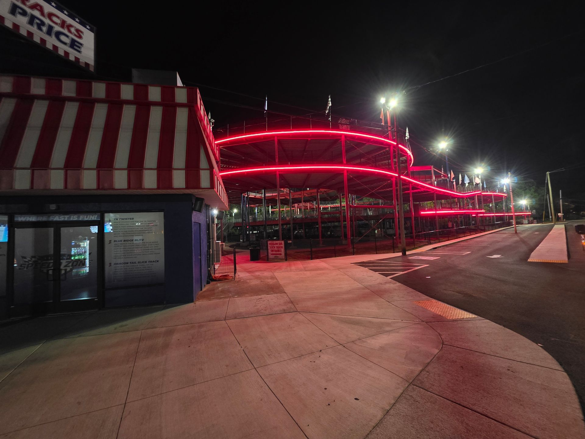 Red neon-lit building at night beside an empty sidewalk and street corner