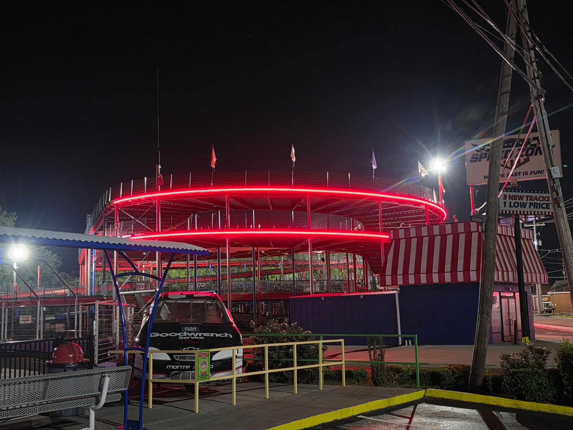 Night scene of a circular building lit with bright red neon, seen behind fencing and parked cars.
