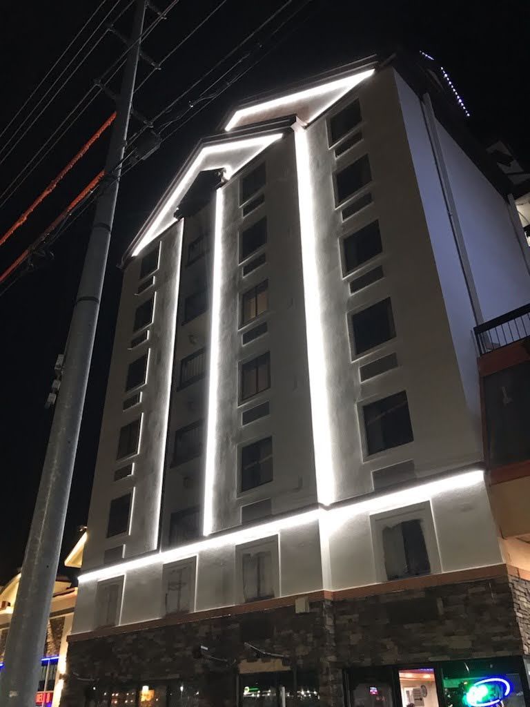 Tall modern building at night with bright white accent lights and a lit ground-floor storefront.