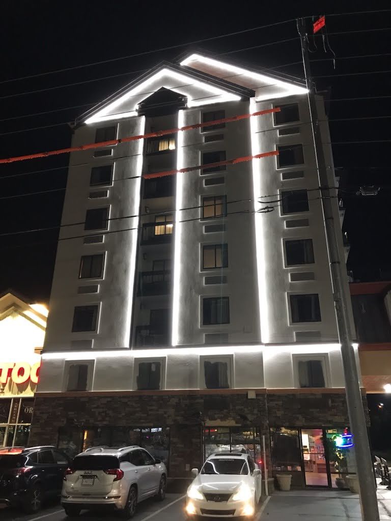 Illuminated modern building at night with white light trim and parked cars below