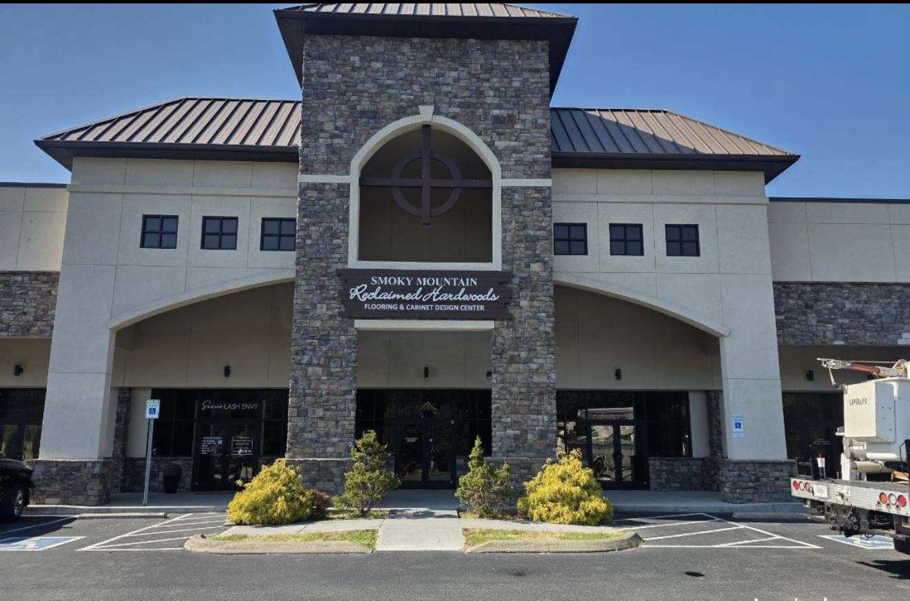 Stone-and-stucco building entrance with arched tower, dark roof, and sign above the doors.
