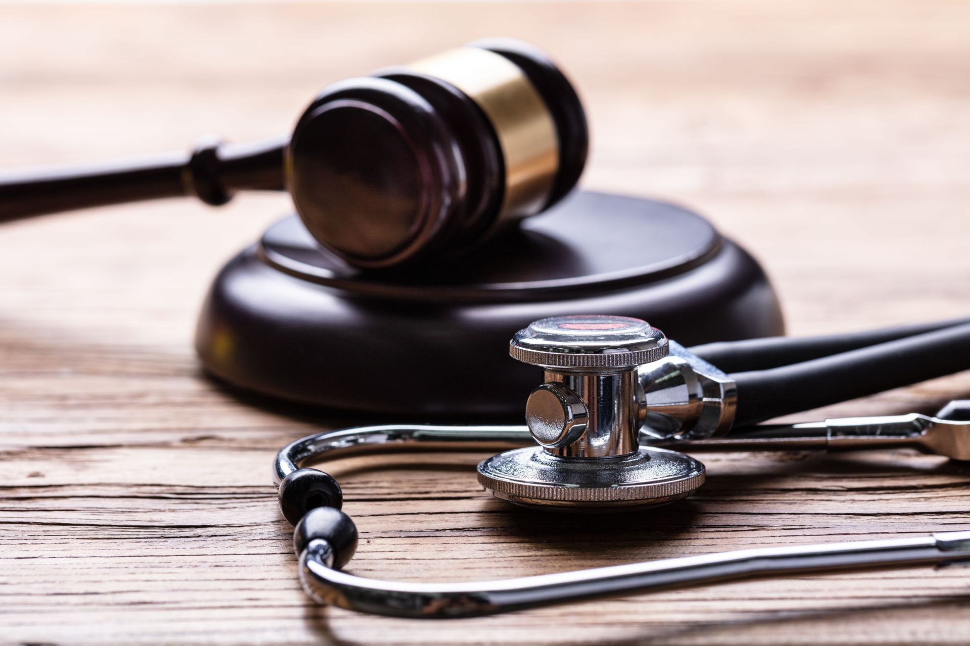 A stethoscope and a judge 's gavel on a wooden table.