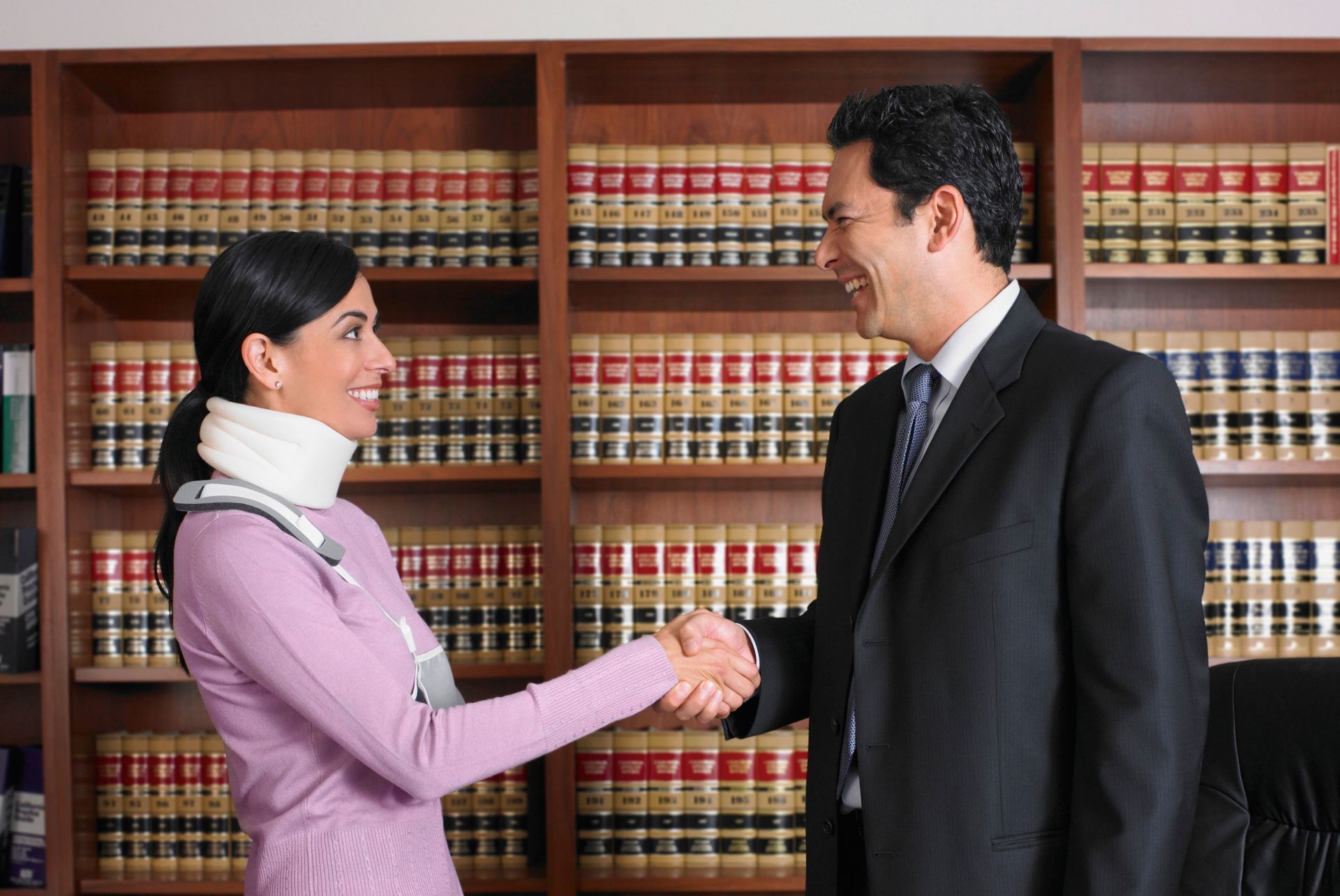 A man and a woman are shaking hands in front of a bookshelf.
