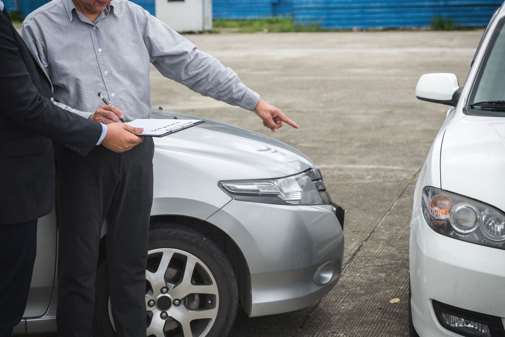 A man is pointing at a car while standing next to another car.