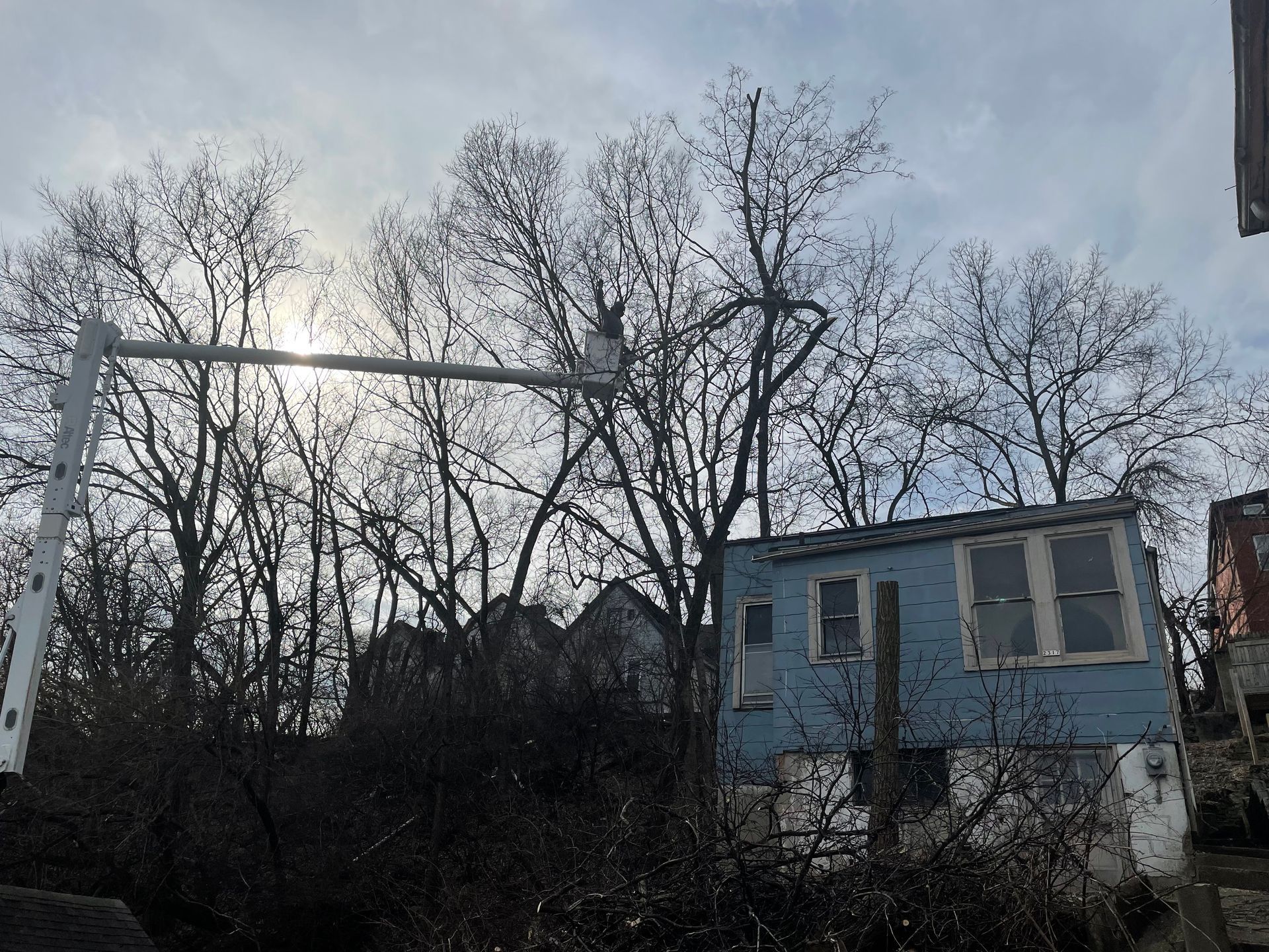 A dilapidated two-story blue house and trees silhouetted against a cloudy sky. A white sign arm extends from the left.