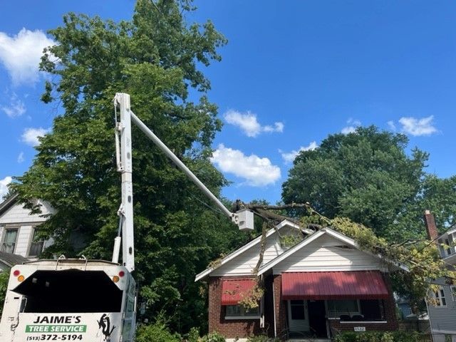 A utility truck with an extended boom working on power lines in front of a house with a damaged roof and red awning. Blue sky.