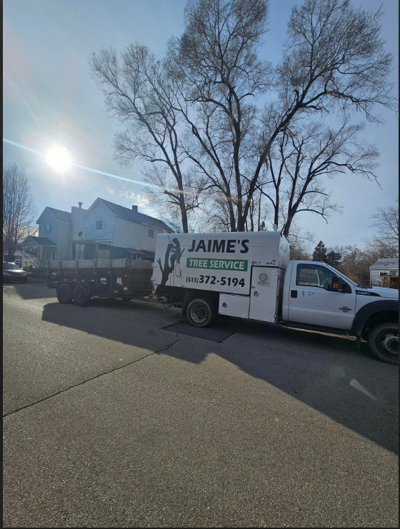 A white truck with a trailer, parked on a street in front of a house; the truck has the logo 