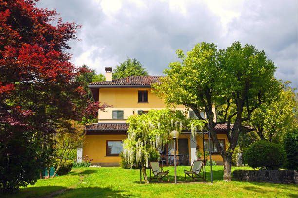 Yellow two-story house with a red maple tree on the left and green trees on the right, lawn in the foreground.