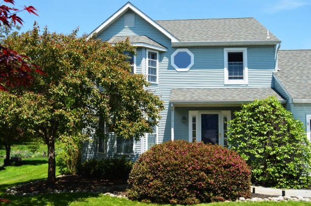 Two-story blue house with grey roof, a vibrant green lawn, and trees.