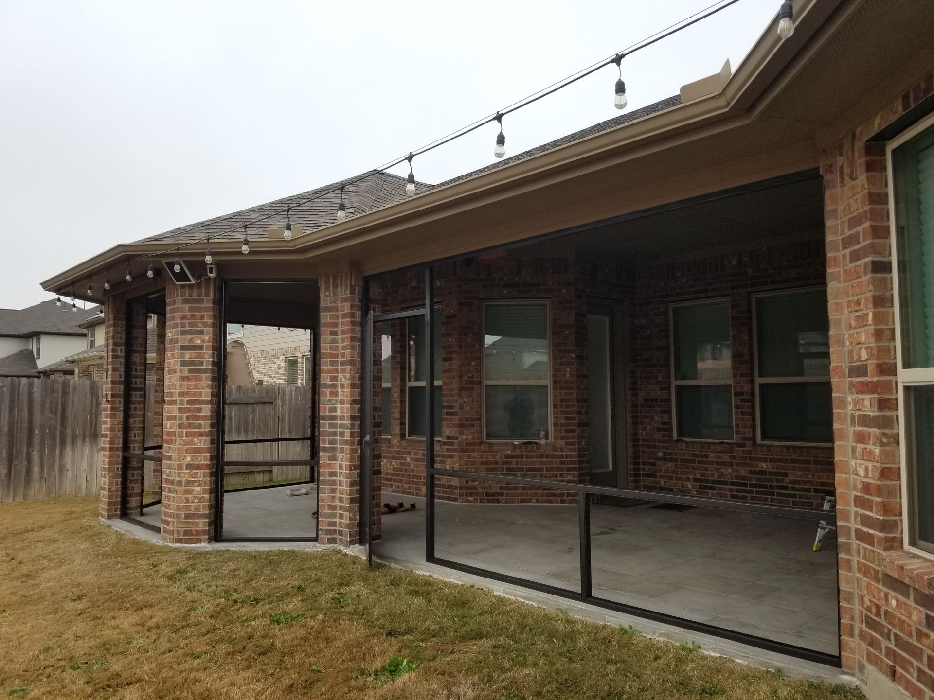 a screened in porch with a brick house in the background
