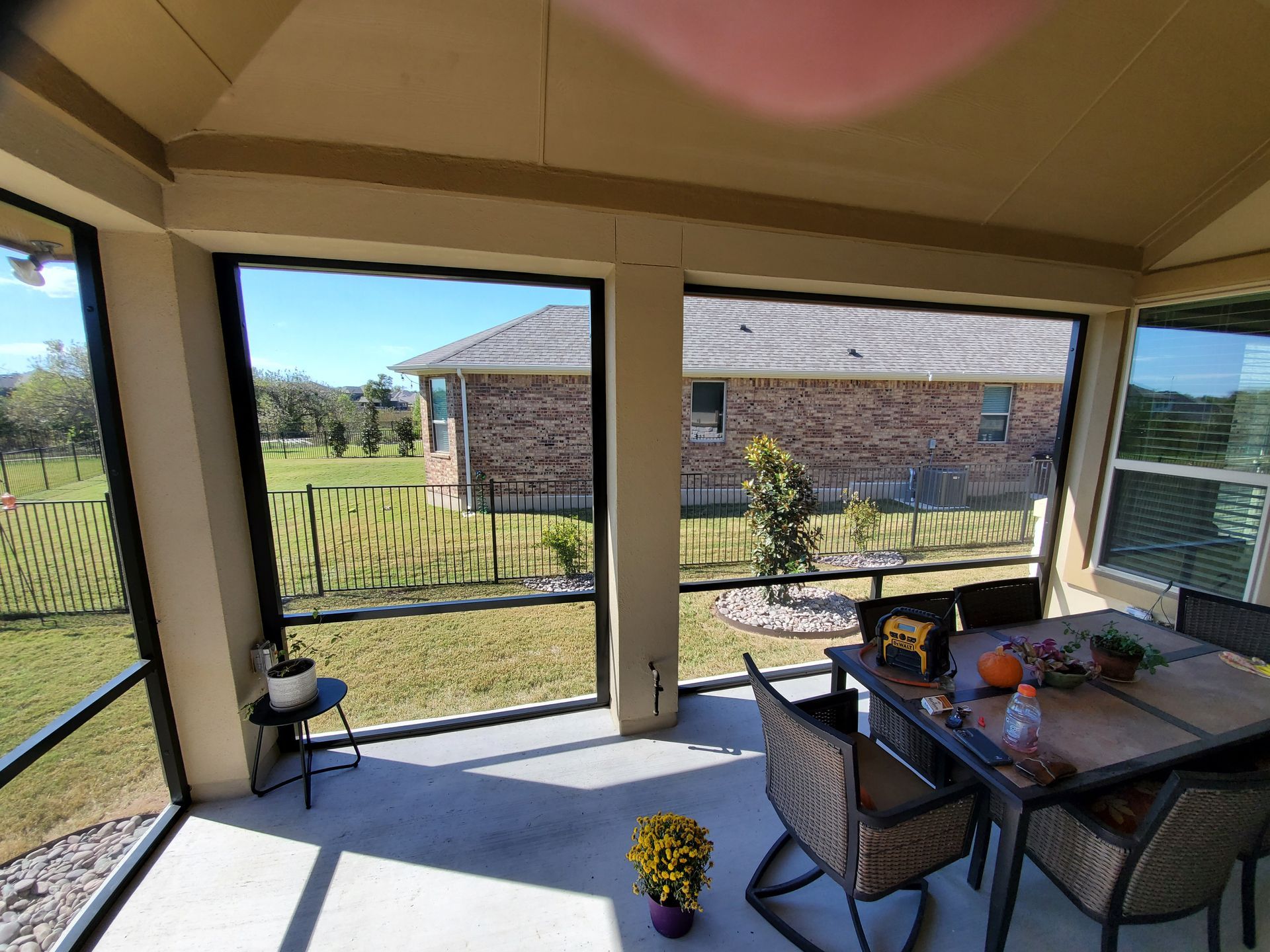 a screened in porch with a table and chairs and a view of a brick house .