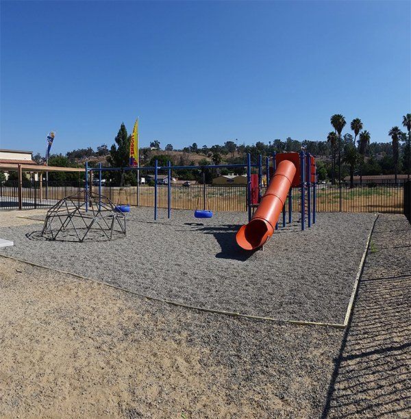 Playground with blue and orange equipment on a gravel surface under a clear blue sky.