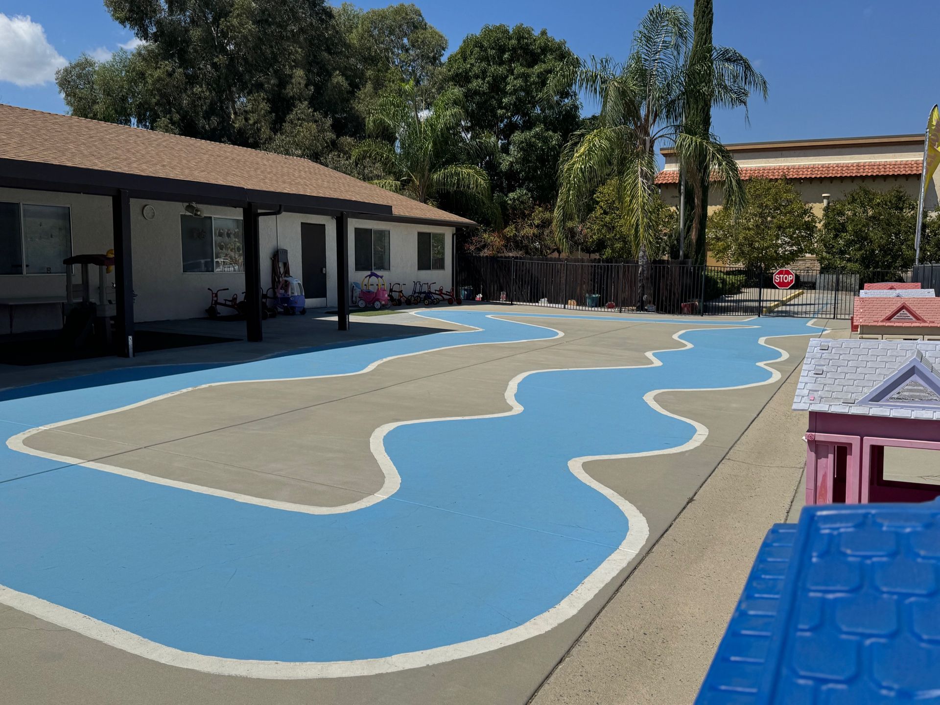 Courtyard with a blue painted river and playhouses; building in background.