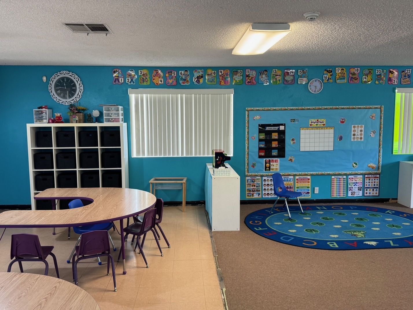 Classroom with teal walls, a U-shaped table, blue rug, and educational decorations.