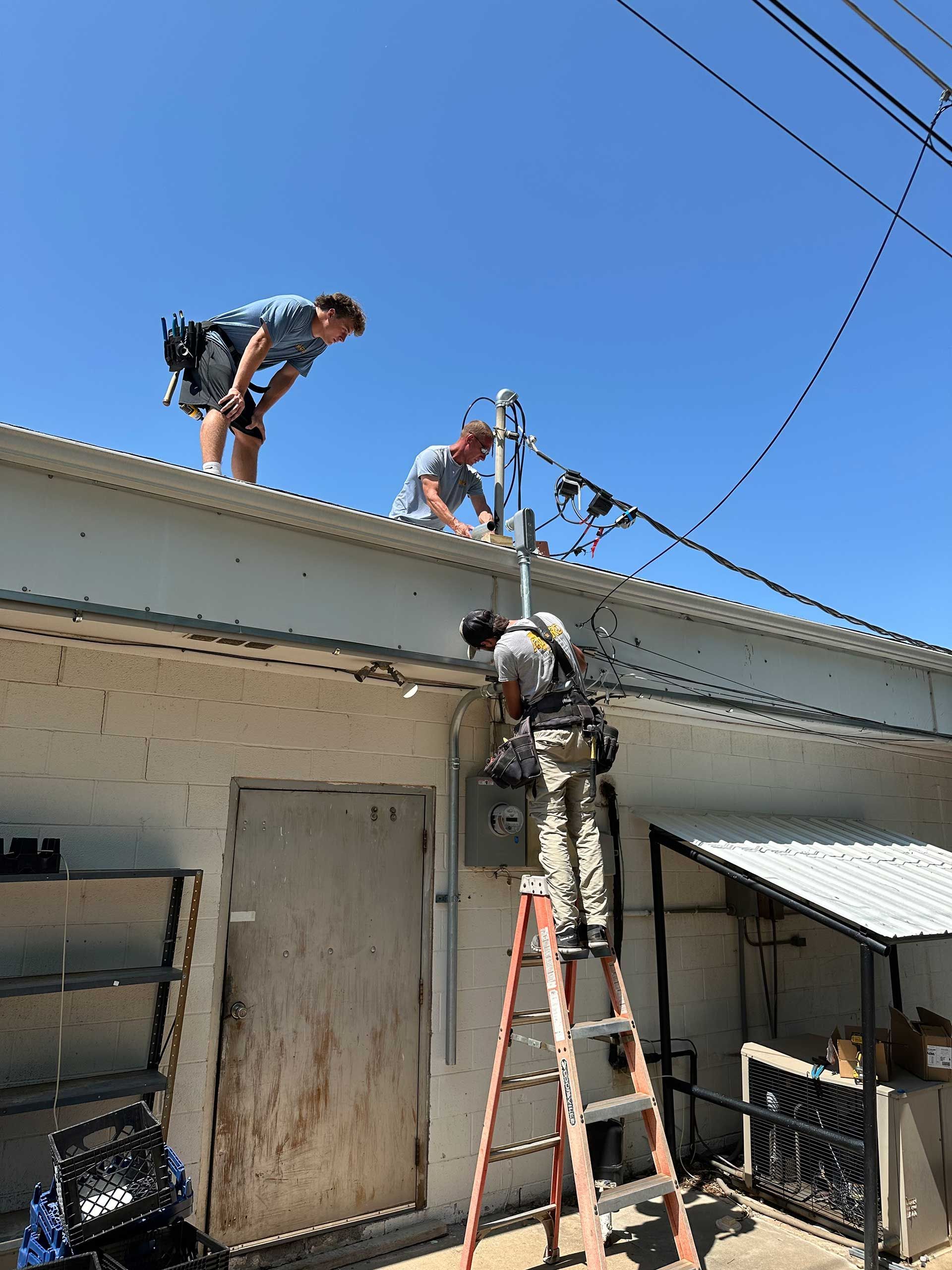 men are working on the roof of a building and a man is on a ladder
